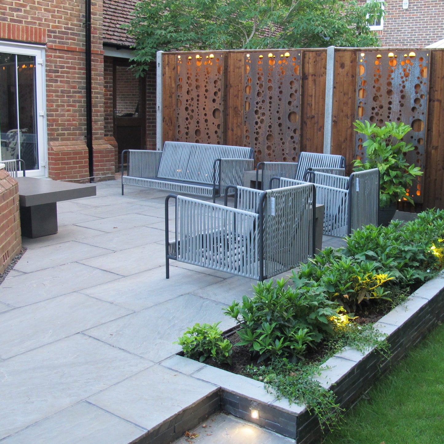 Modern garden with paved patio, outdoor furniture, and decorative plants.